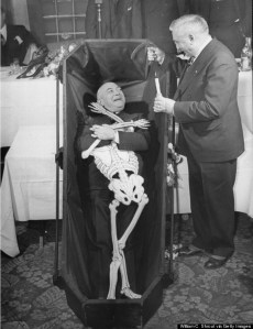 A man laying in a coffin with a paper sk